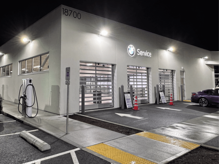 BMW Service center at night, with brightly lit garage doors, prominent signage, and EV charging stations.