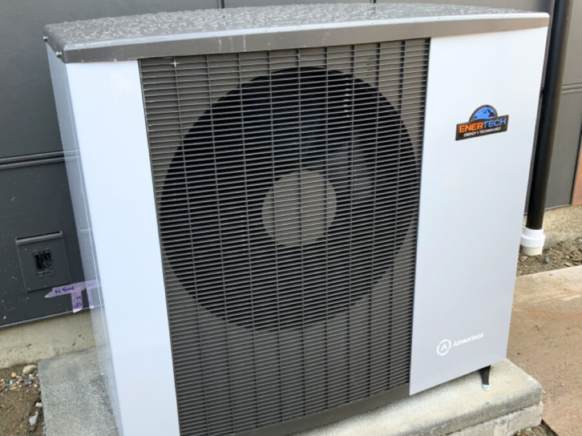 Enertech air to water heat pump sitting on concrete block outside of home