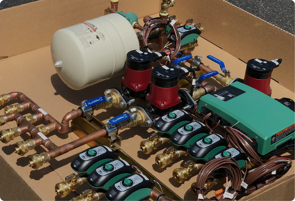 New radiant heating system components: copper manifolds, multiple red circulating pumps, green electronic controls, and a white expansion tank.