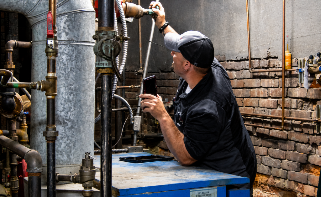 Boiler repairman checking valves on piping above boiler