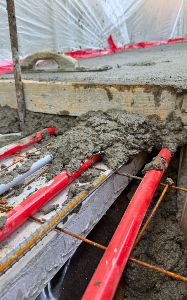 Close-up of all the elements of the layers: foundation, moisture barrier, wire mesh, PEX tube, rebar, and concrete.