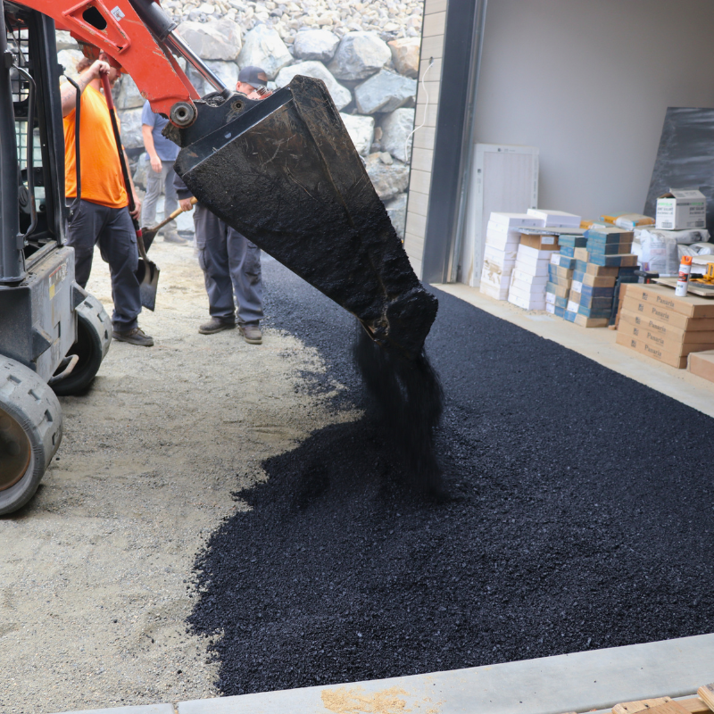 Hot asphalt is being poured on the driveway in the snowmelt installation